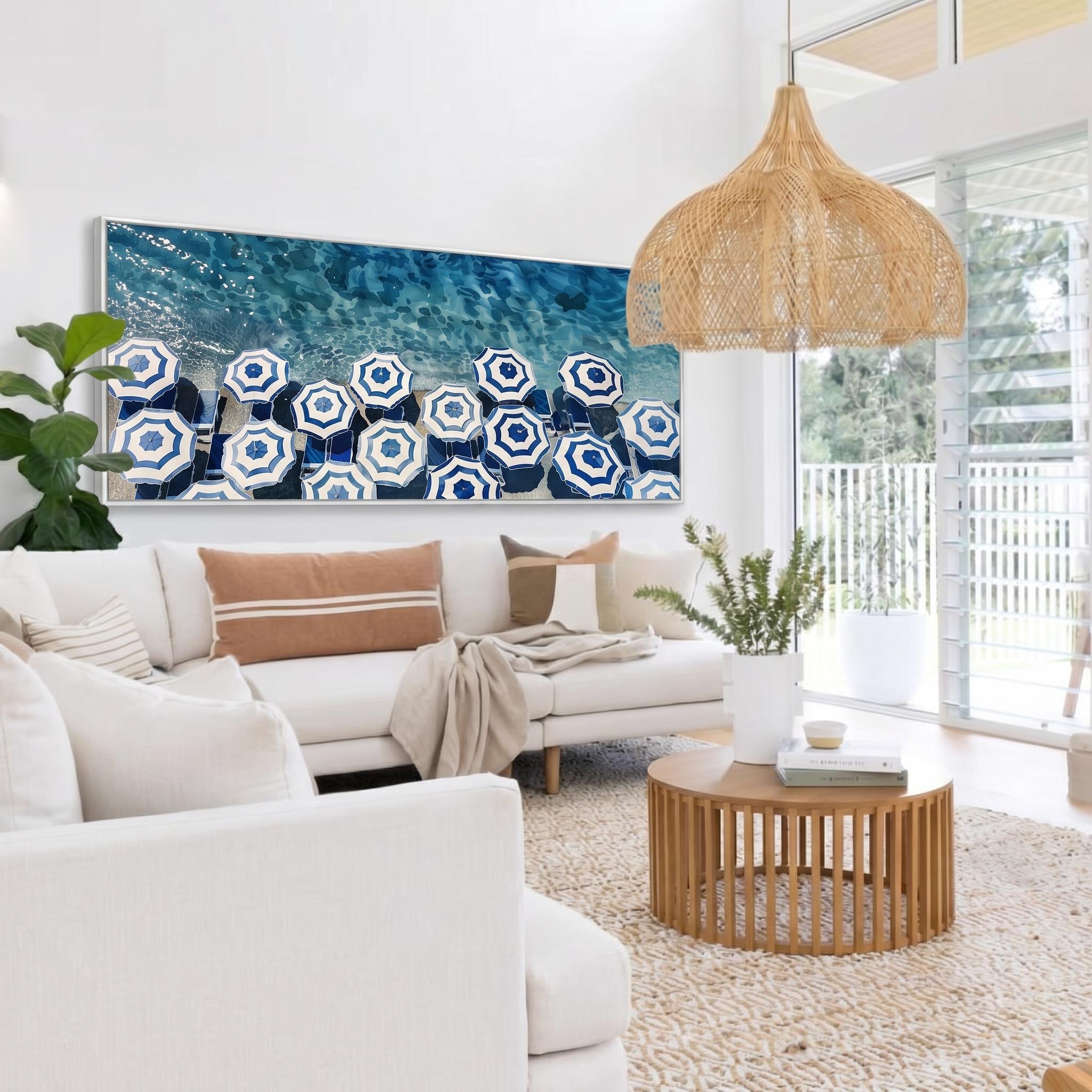 May include: A living room with a white sofa, throw pillows, and a round wooden coffee table. A large framed artwork depicts blue and white beach umbrellas. A woven pendant light hangs from the ceiling.